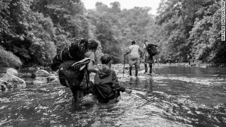 A Venezuelan woman guides her son through knee-high water, his dinosaur toy stuffed safely in his sweatshirt. She&#39;s hoping to get them to the US, to be reunited with her husband.