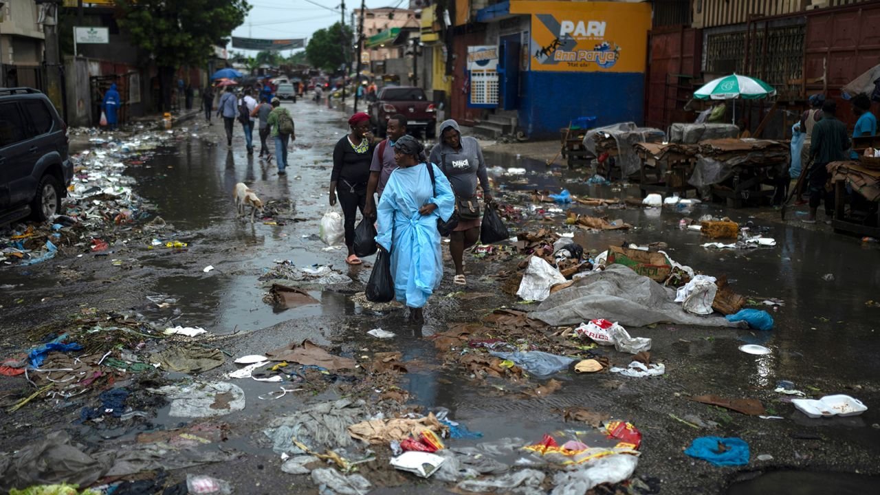 People make their way through puddles while walking in the middle of a street littered with garbage following heavy rains in Port-au-Prince.