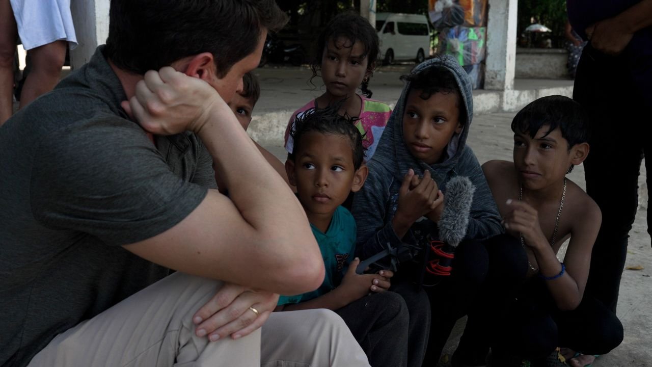 Joandry, 6, center holds the microphone while his sister Sofia, 12, and cousin Mathias, 9, talk to CNN's David Culver in Ciudad Hidalgo, Mexico, on the banks of the Suchiate River.